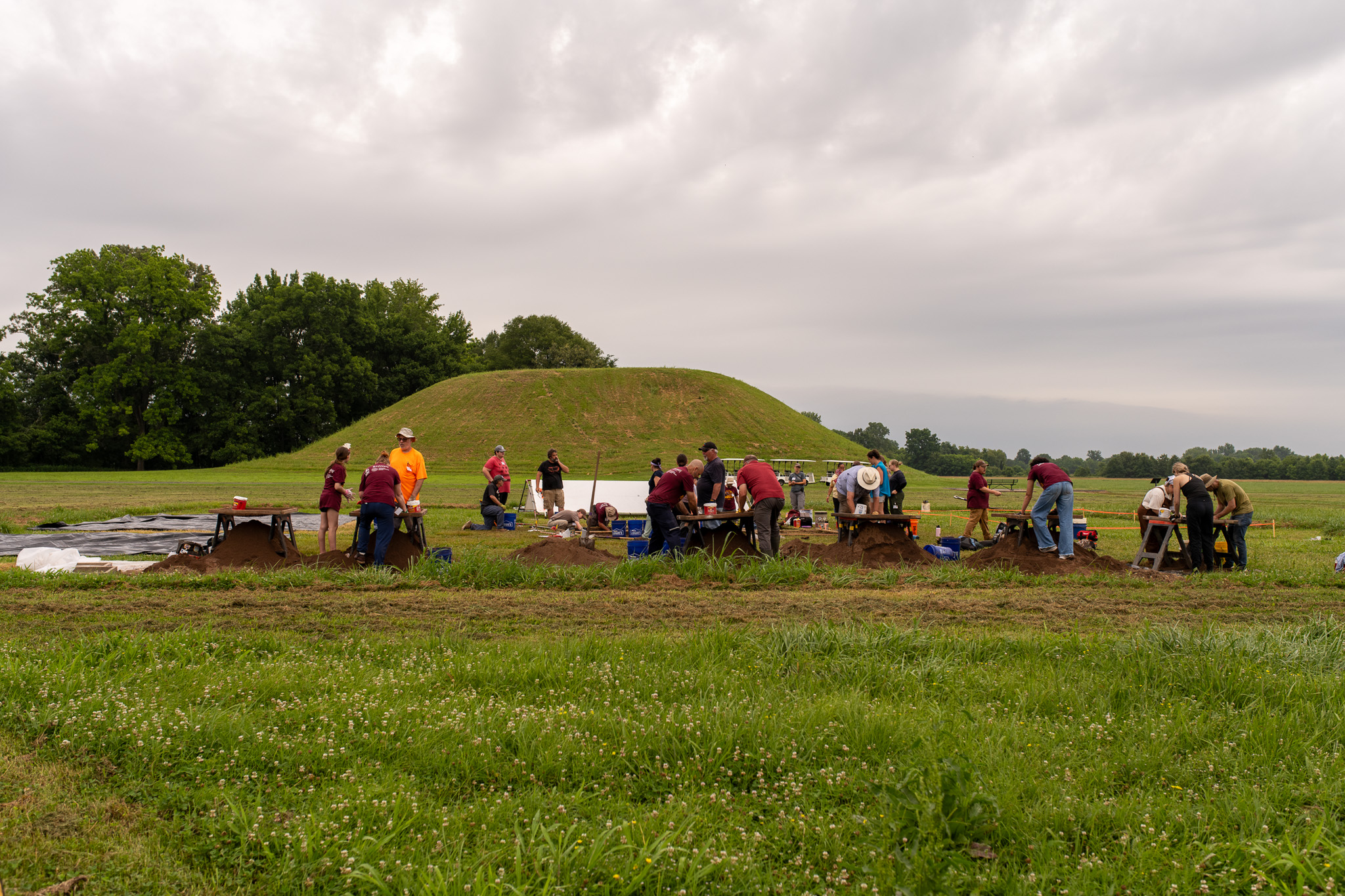 large earthen mound with archeologist crew excavating